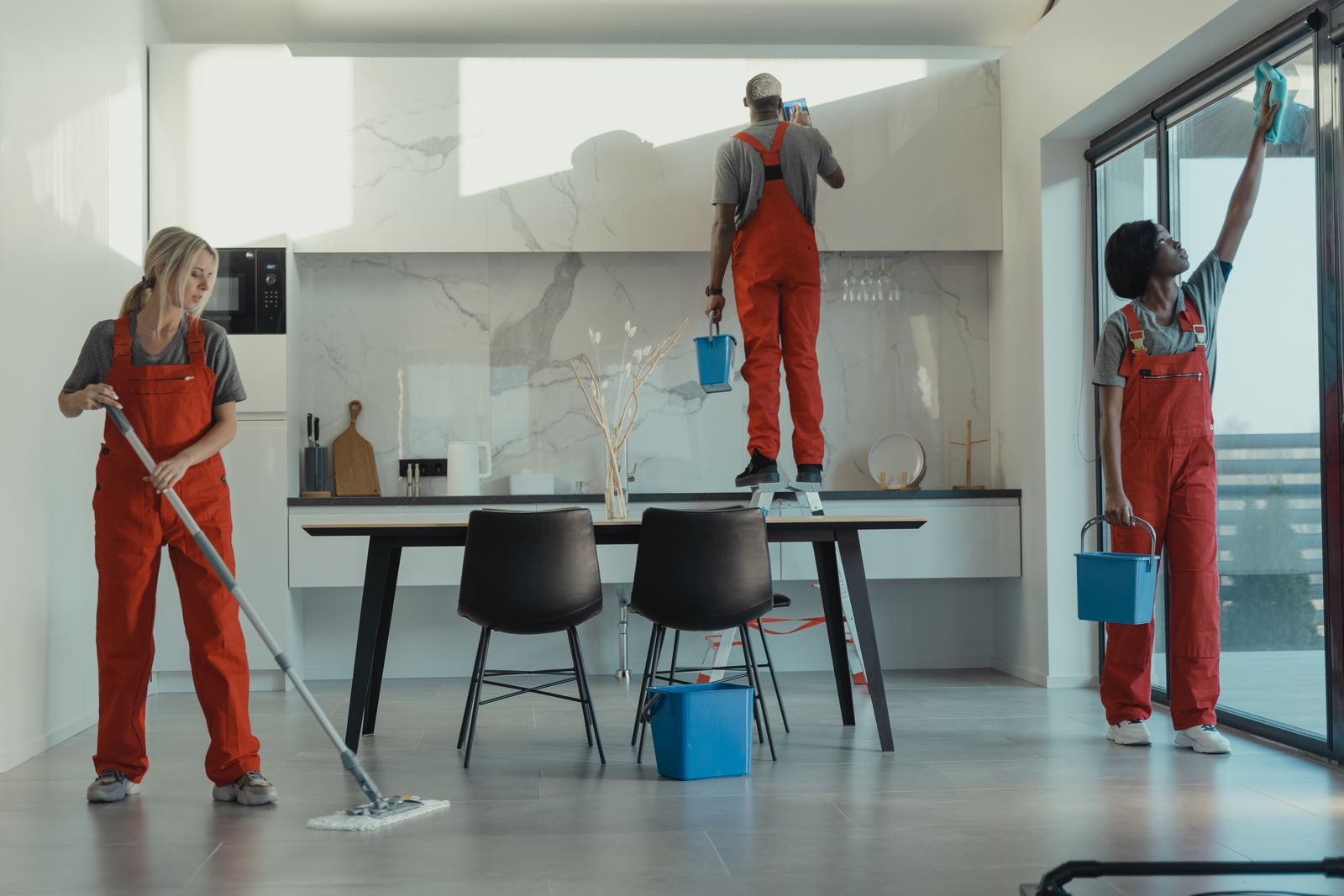Group of cleaners in red uniforms mopping and wiping glass in a modern dining room