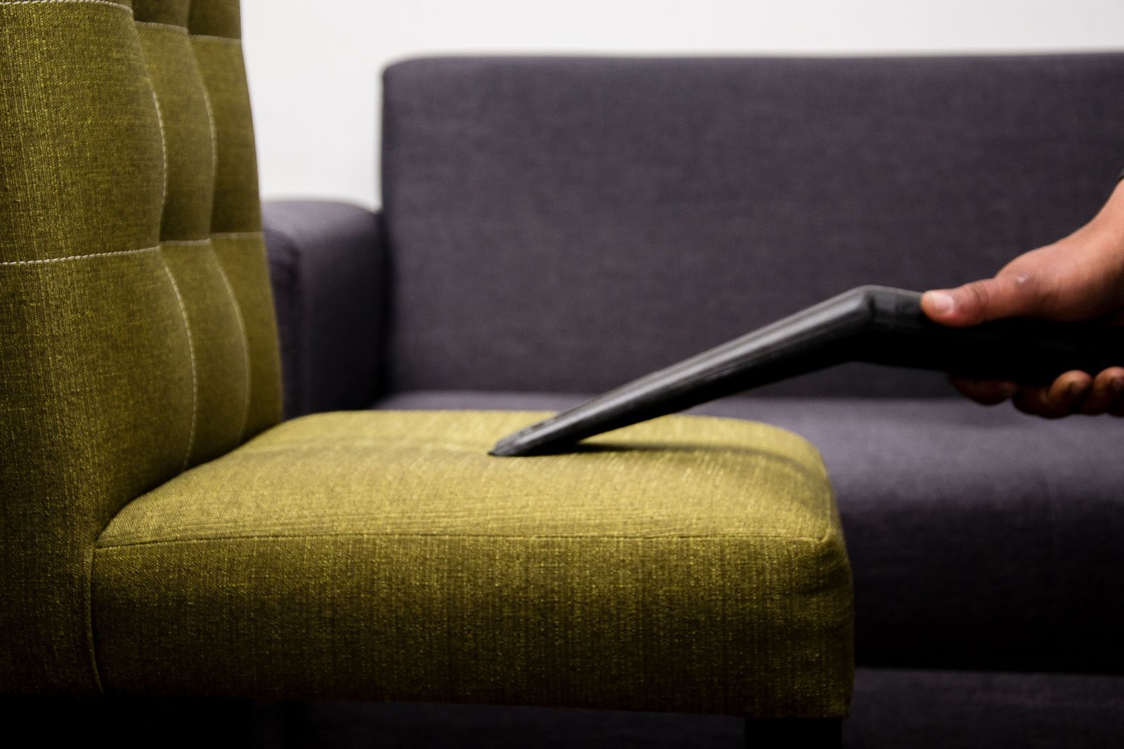 Close-up of a person vacuuming a modern sofa chair indoors, highlighting cleaning service